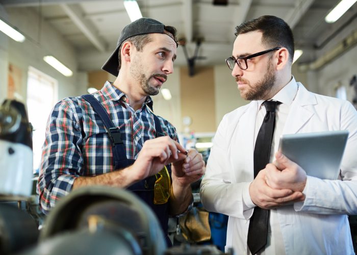 Waist up portrait of repairman talking to factory worker standing by machine units in workshop, copy space